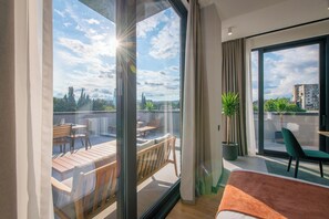 Habitación de hotel moderna con un balcón grande, un sofá, una mesa de comedor y una planta en maceta.