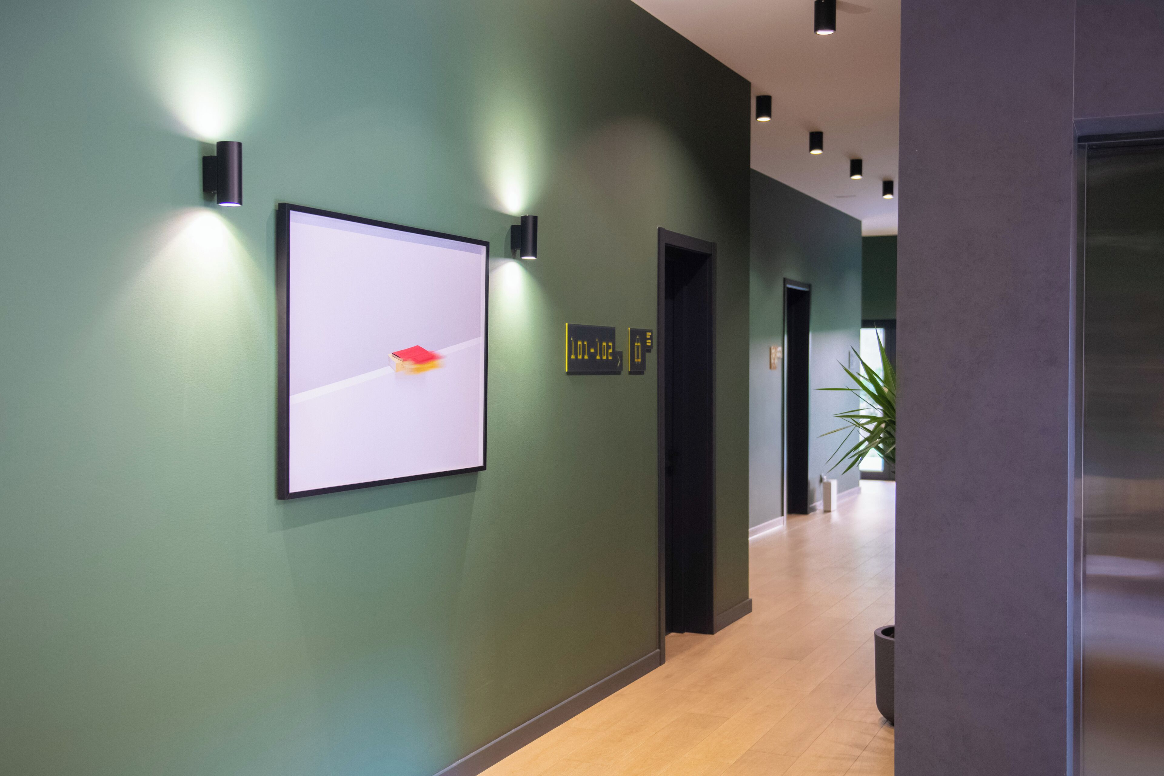 A hallway with a framed artwork on the wall, a digital clock, and a potted plant.