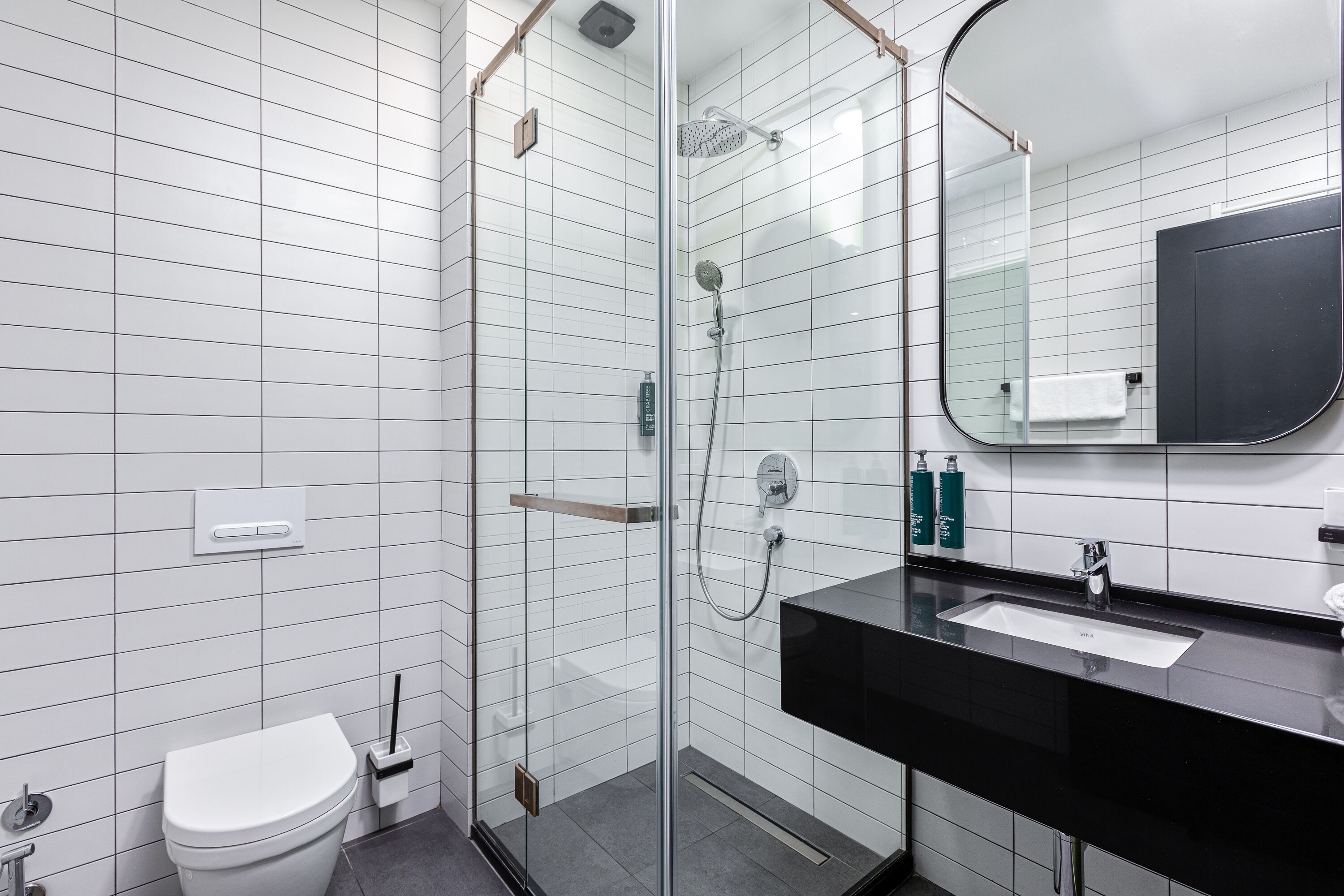 Une salle de bain moderne avec une douche à parois de verre, un lavabo noir et des toilettes blanches.