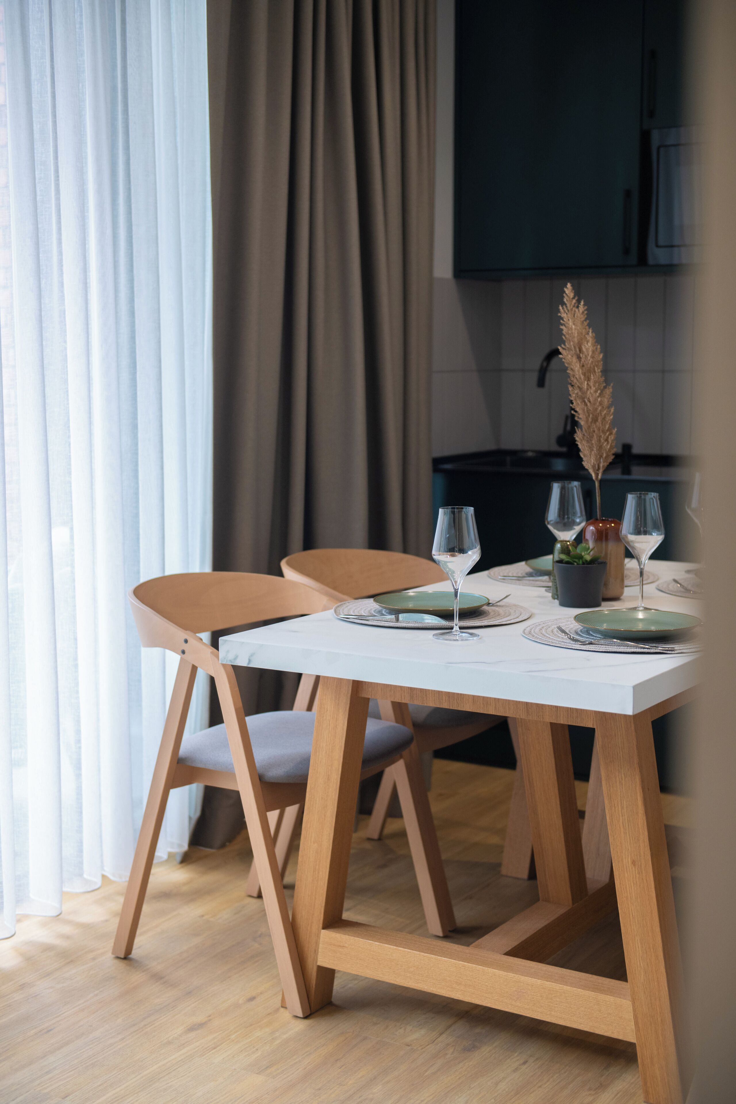 Een eettafel met twee stoelen, een potplant en wijnglazen.