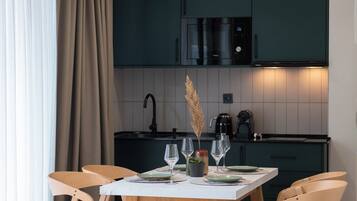 Una cocina moderna con armarios oscuros, una encimera blanca y una zona de comedor con sillas de madera y una mesa preparada para dos.