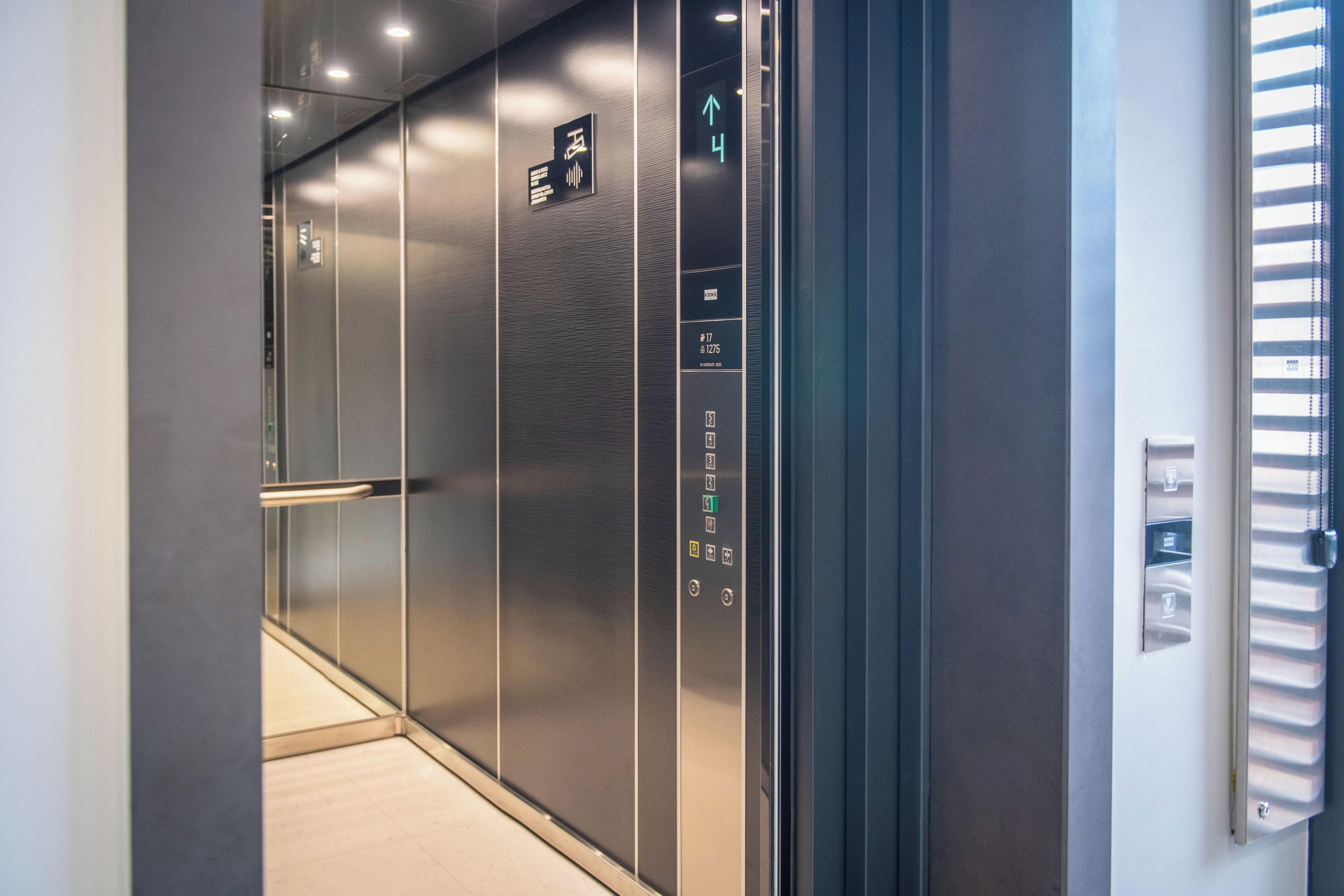 A modern elevator interior with metallic walls, a digital display showing the floor number, and a handrail.