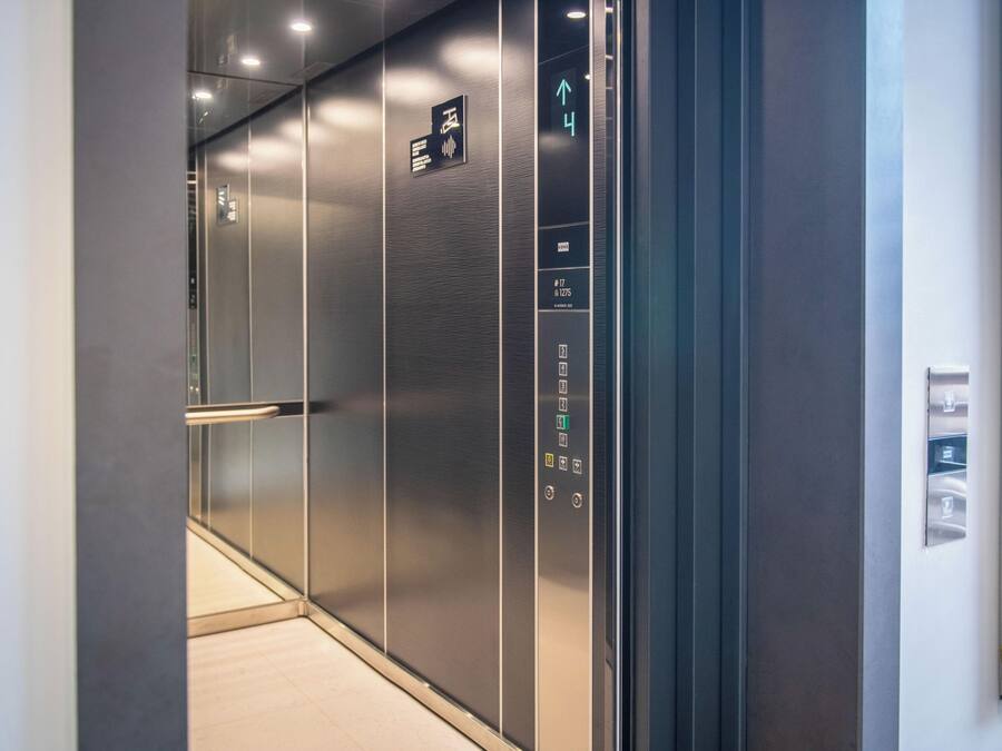 A modern elevator interior with metallic walls, a digital display showing the floor number, and a handrail.