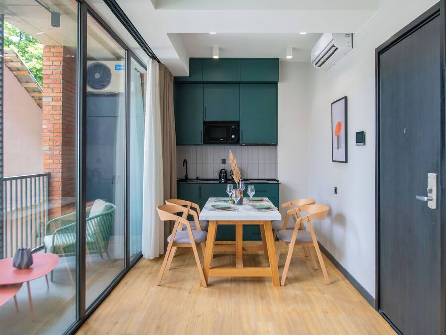 Een moderne keuken met groene kastjes, een magnetron en een eethoek met een tafel en stoelen.