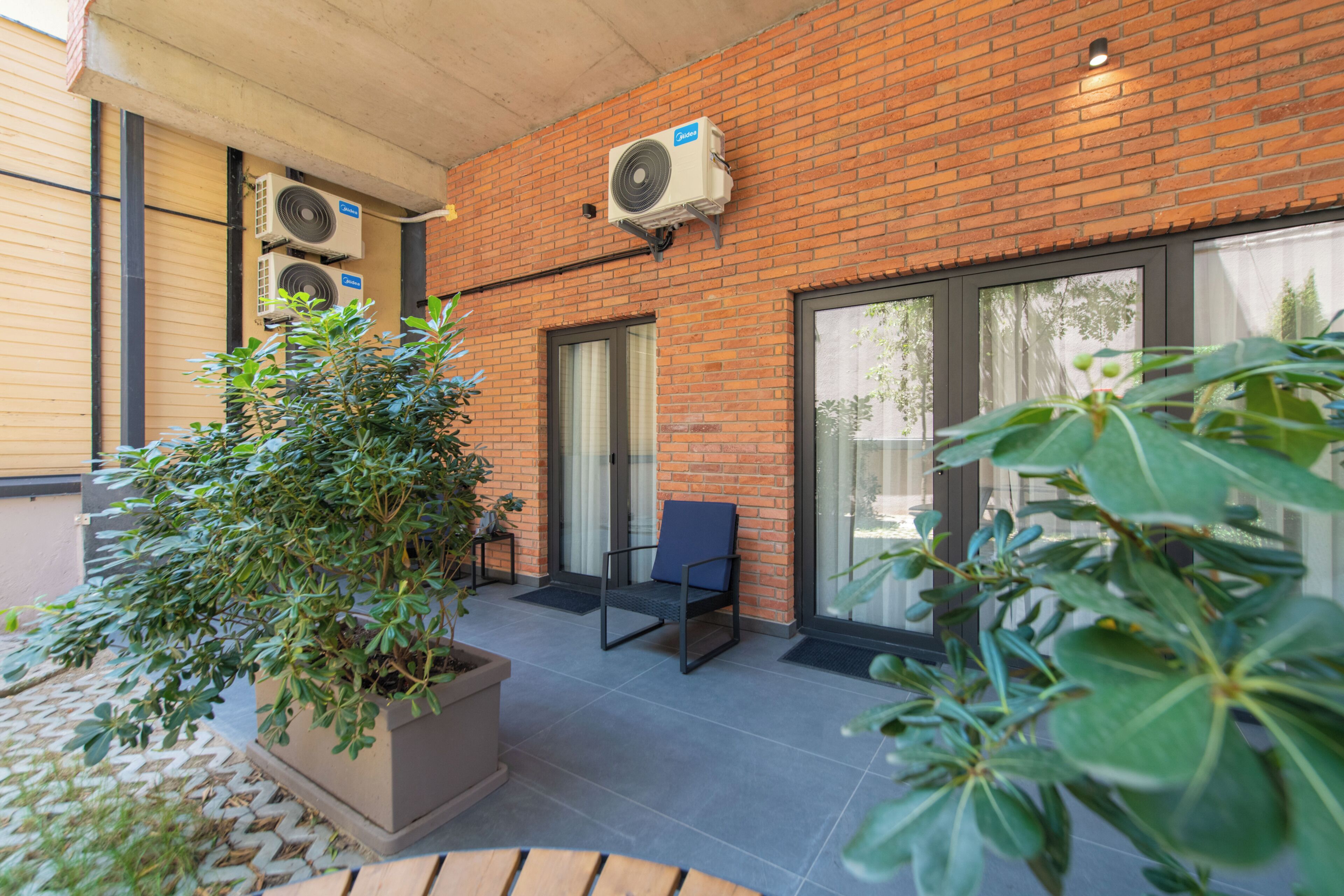 A brick building with air conditioning units, a potted plant, a chair, and a door.