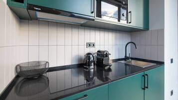 A modern kitchen with teal cabinets, a black countertop, a coffee maker, and a kettle.