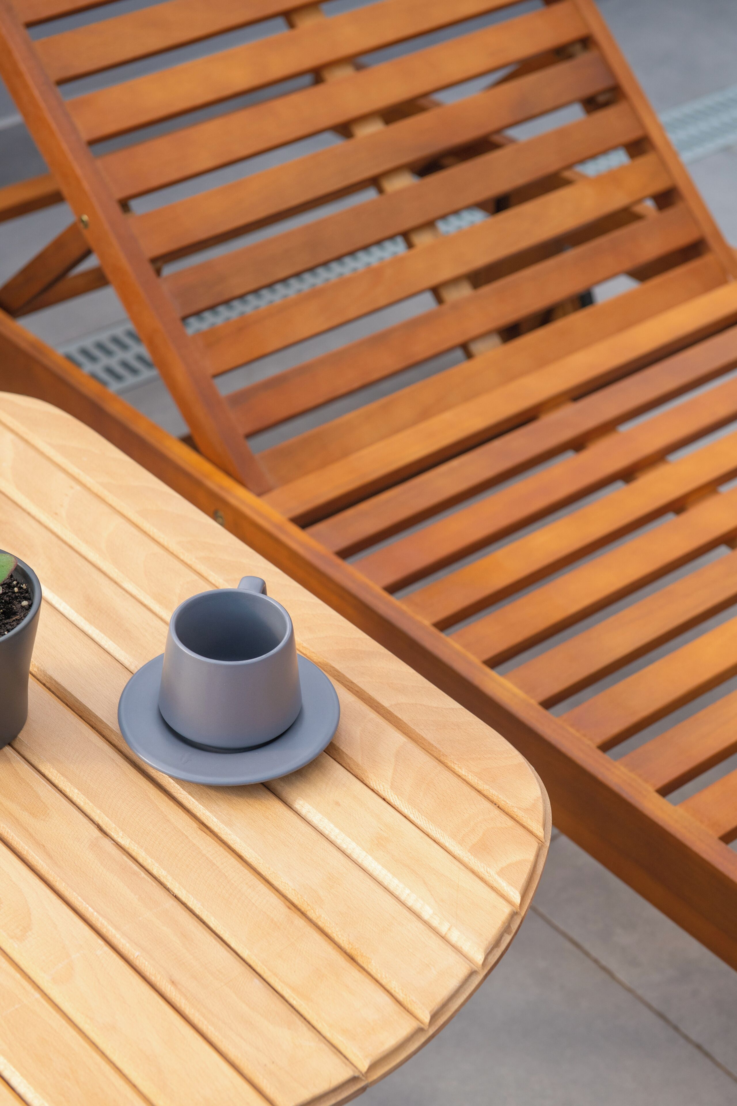 A round wooden table with a gray cup and saucer, and a potted plant on it.