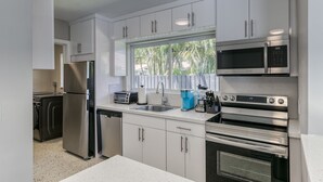 Een moderne keuken met roestvrijstalen apparatuur, witte kasten en een raam met uitzicht op palmbomen.