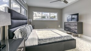 Een moderne slaapkamer met een groot bed, een televisie, een dressoir en een raam met uitzicht op palmbomen.