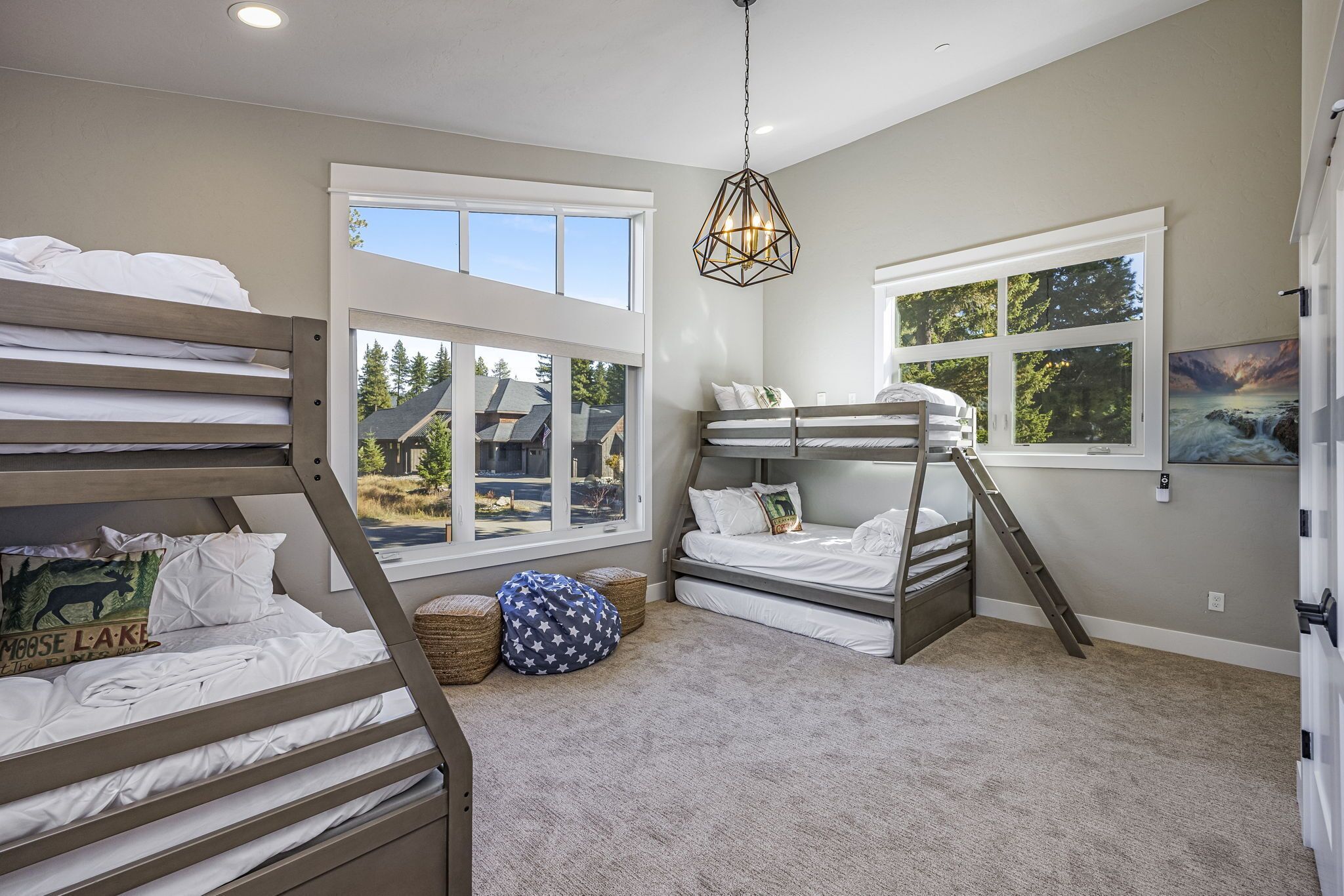 A bedroom with two bunk beds, large windows, a hanging light fixture, and a view of a house.