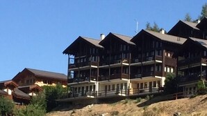A multi-story building with balconies, situated on a hillside with sparse vegetation. - Exterior : Apartment on the lower ground floor of a building, for 4 people close to the hotel/restau (St-Luc)