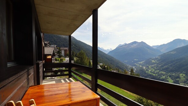 A wooden table and chairs on a balcony with a mountain view. - Exterior : Apartment on the lower ground floor of a building, for 4 people close to the hotel/restau (St-Luc)