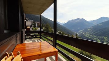 Une table et des chaises en bois sur un balcon avec vue sur la montagne.