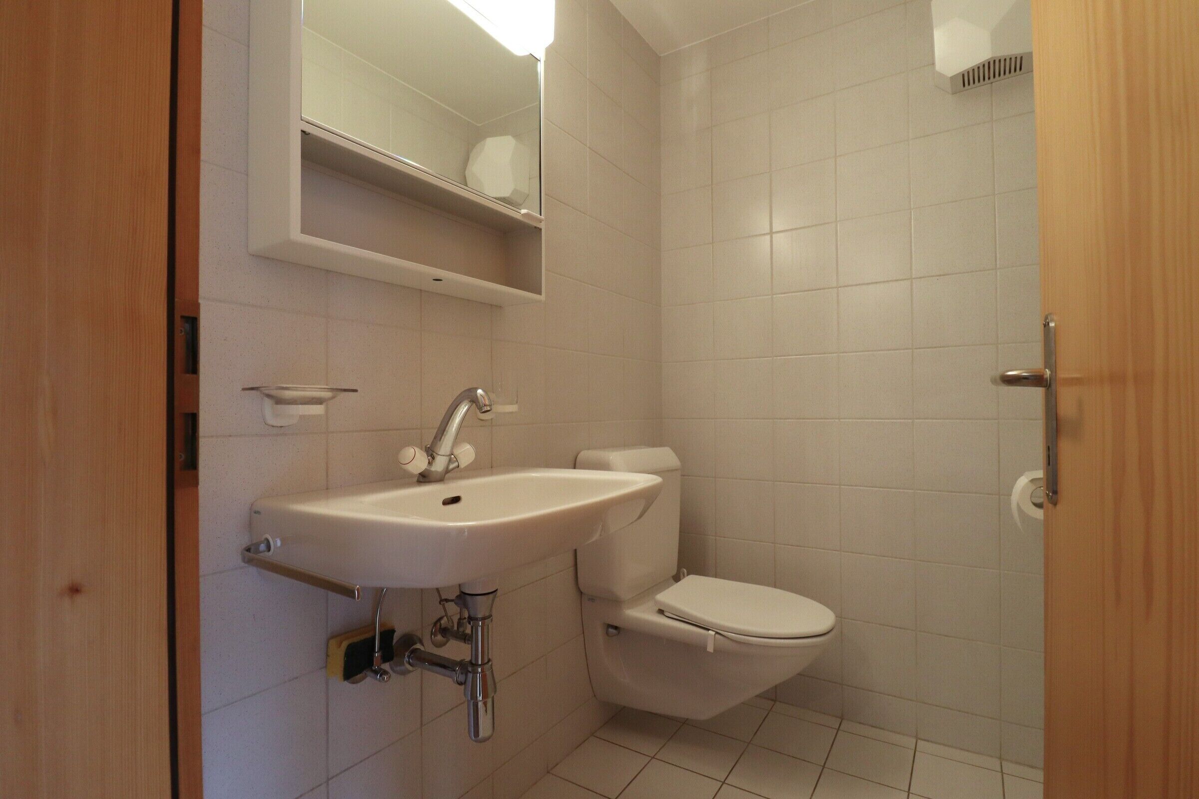 Une petite salle de bain avec un lavabo blanc, des toilettes et un miroir au-dessus du lavabo.