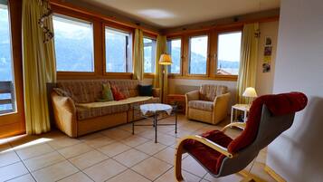 Un salon chaleureux avec un canapé, un fauteuil à bascule, une petite table et de grandes fenêtres donnant sur une vue imprenable sur les montagnes.