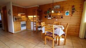 A wooden-paneled kitchen with a dining table and chairs, a built-in oven, and a hanging light fixture. - Exterior : Apartment on the lower ground floor of a building, for 4 people close to the hotel/restau (St-Luc)