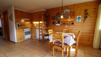 Une cuisine aux murs lambrés, avec une table et des chaises, un four encastré et un luminaire suspendu.