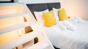 Une chambre d’hôtel moderne, dotée d’un lit, de draps blancs, d’une tête de lit et d’un escalier avec un éclairage intégré.