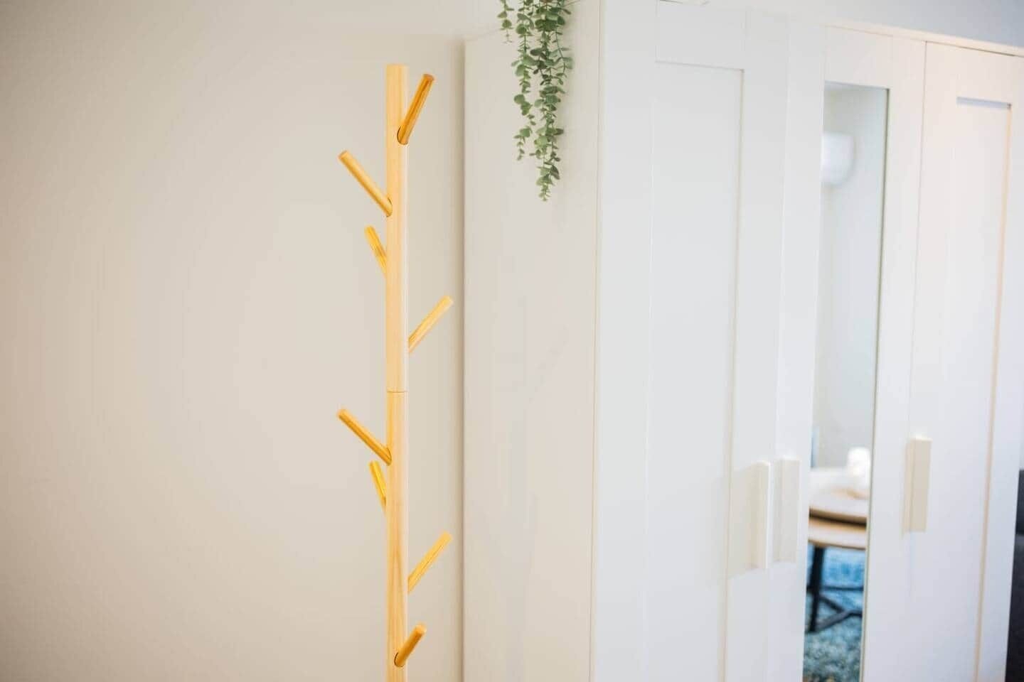 Un muro bianco con un appendiabiti in legno e una pianta sospesa.