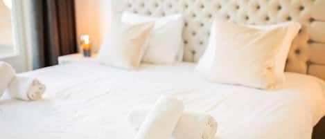 A neatly made bed with white linens and pillows, a tufted headboard, and a bedside lamp.