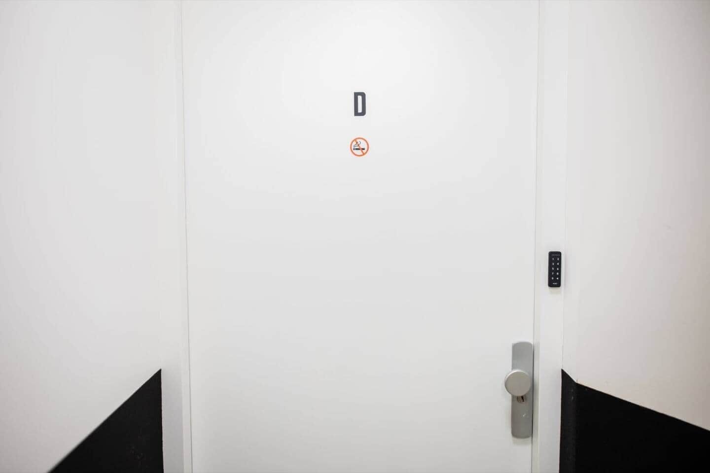 A white door with a no-smoking sign, a keypad lock, and a door handle.