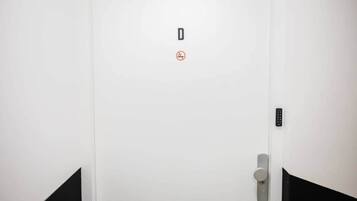 A white door with a no-smoking sign, a keypad lock, and a door handle.