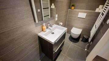 A modern bathroom with a white sink, dark tiles, a toilet, and a small plant.
