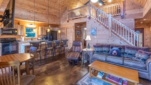 Une cabine spacieuse avec un intérieur en bois, un coin repas, un salon doté d’un canapé et d’une table basse, et une cuisine équipée d’appareils électroménagers modernes.