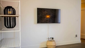 Una sala de estar moderna con un televisor de pantalla plana montado, una estantería blanca con cestas decorativas y una cesta tejida en el suelo.