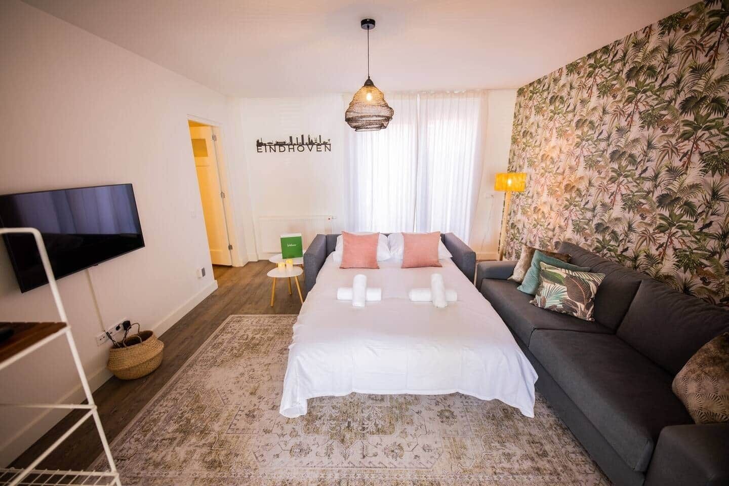 Ein modernes Hotelzimmer mit einem großen Bett, einer Couch, einem Flachbildfernseher, einem Wandbild und tropischen Tapeten.