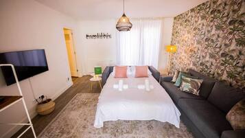 Ein modernes Hotelzimmer mit einem großen Bett, einer Couch, einem Flachbildfernseher, einem Wandbild und tropischen Tapeten.