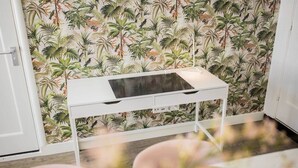 Una habitación con un escritorio blanco frente a una pared con papel tapiz tropical.