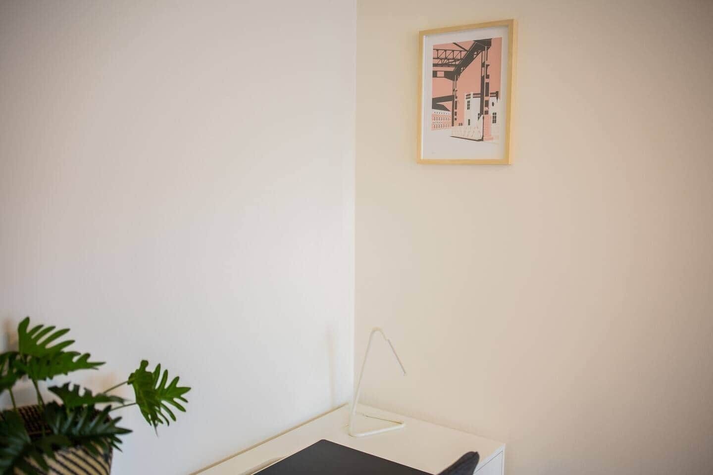Una habitación minimalista con un escritorio, un cuadro en la pared y una planta en maceta.