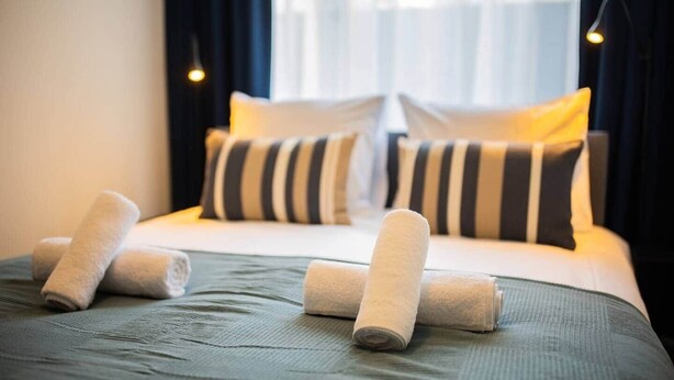 Una cama bien tendida con almohadas a rayas y toallas enrolladas.