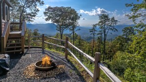 Eine Holzdiele mit Feuerstelle mit Blick auf eine gebirgige Landschaft.