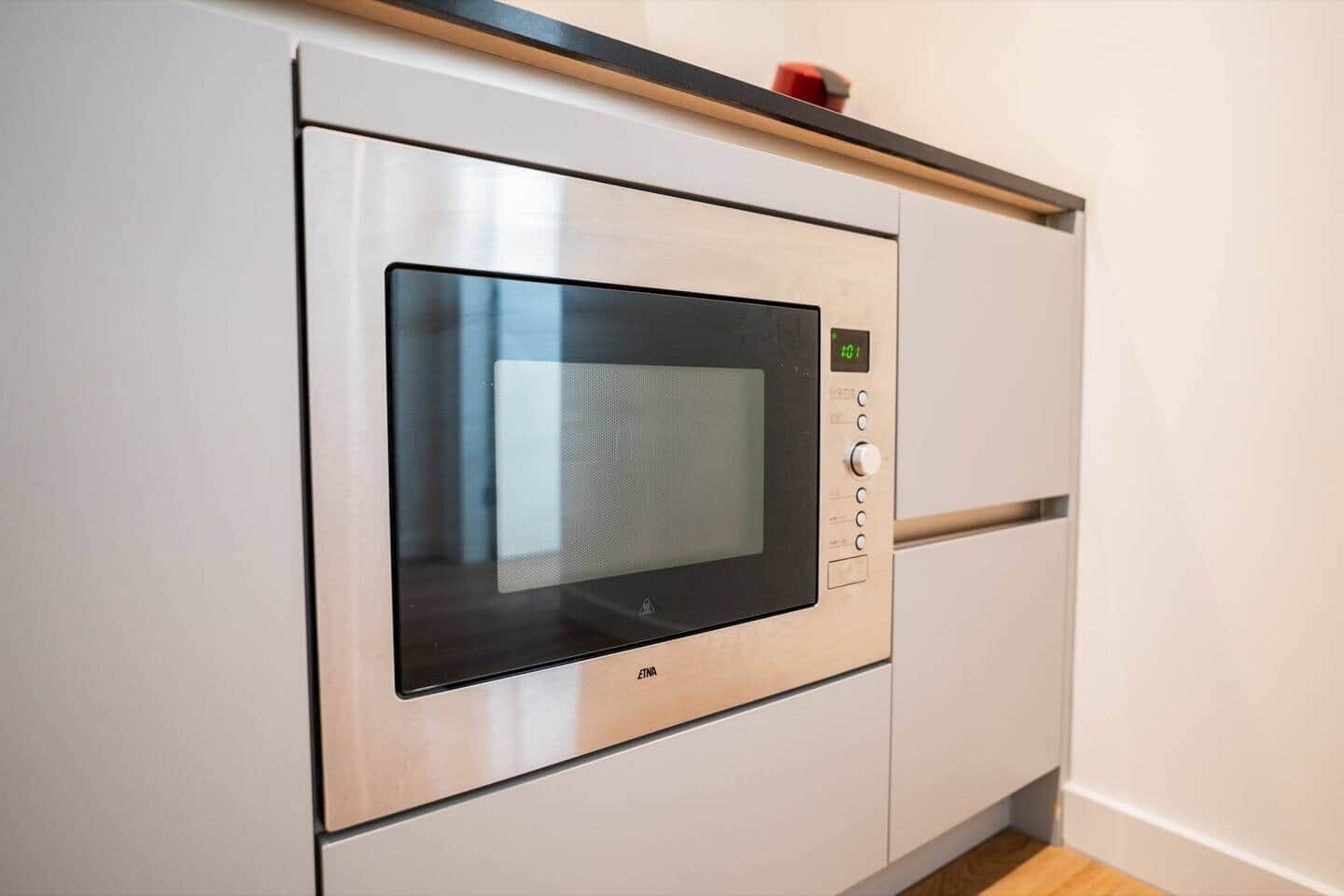 Une cuisine équipée d’un four à micro-ondes encastré, d’un four en acier inoxydable et d’une lumière rouge de signalisation d’urgence.