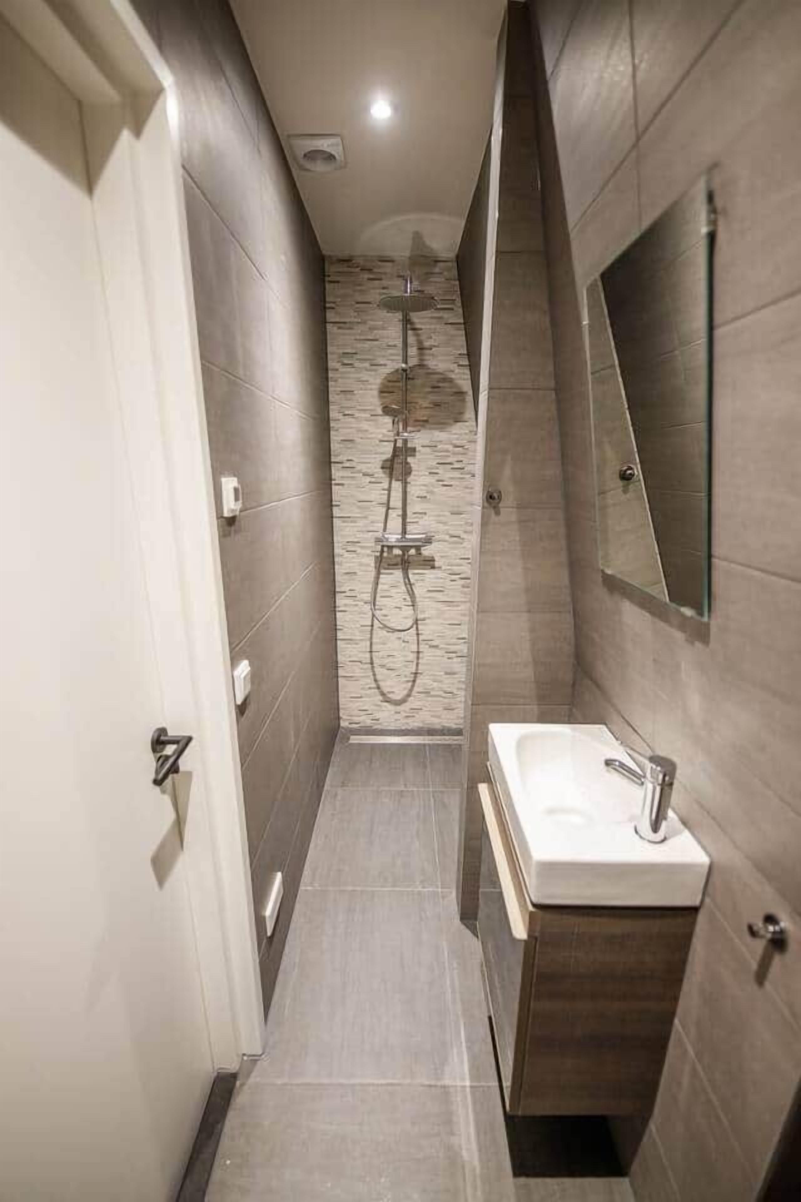 Bany estret amb dutxa, un lavabo i un mirall.