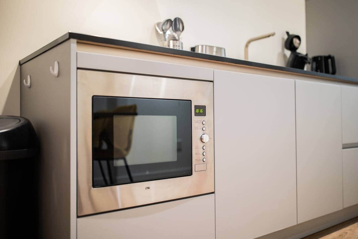A kitchen with a built-in microwave, a trash bin, and a coffee maker on the countertop.
