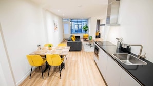 A modern kitchen with a black countertop, stainless steel sink, and a dining area with yellow chairs and a wooden table. - Great 95m2 Two-Bedroom Apartment (WE-39) (Tiel)