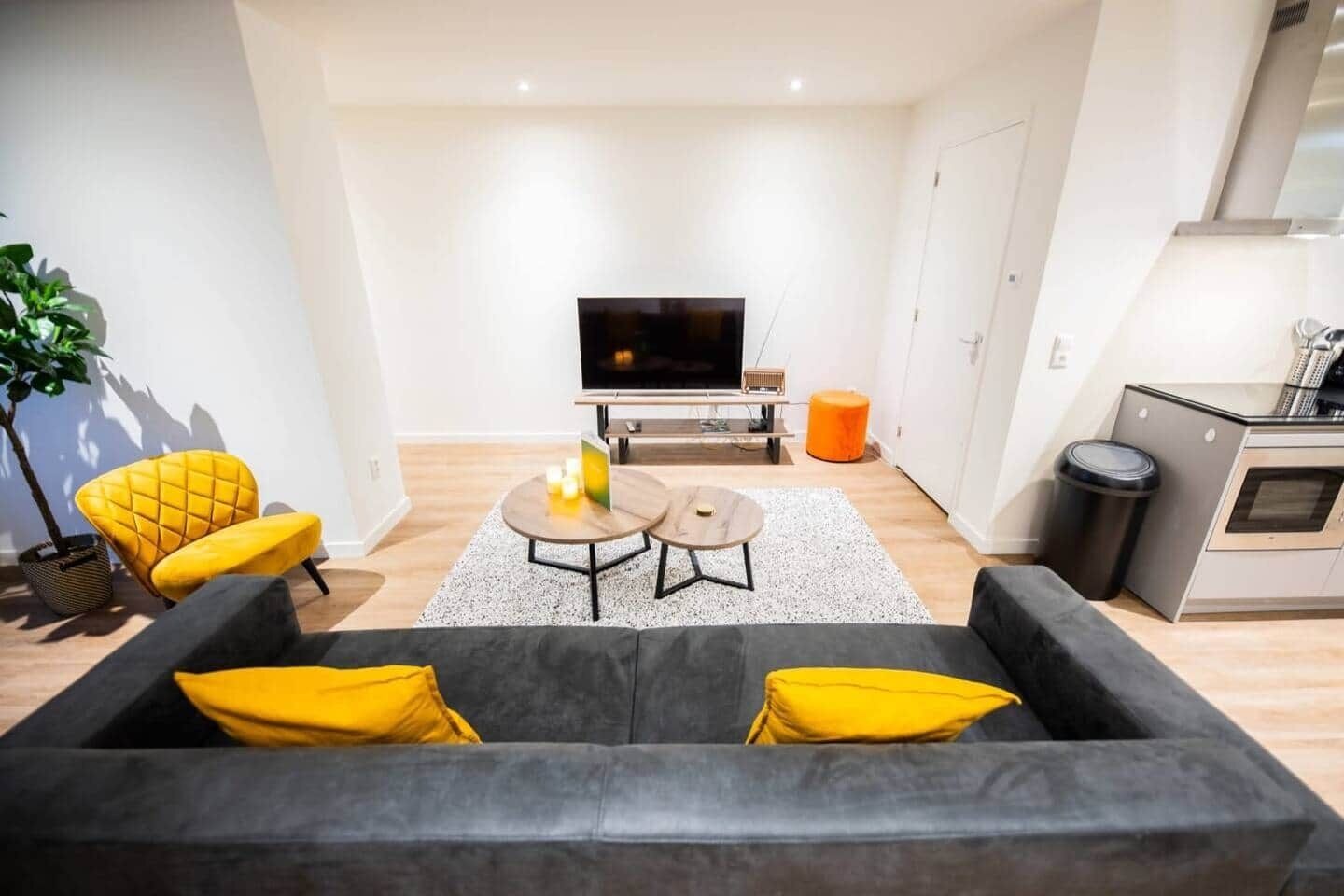 Ett modernt vardagsrum med en soffa, två soffbord, en tv och en köksdel.
