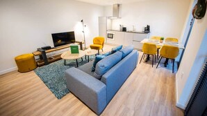 A modern living room with a sofa, yellow chairs, a TV, and a dining area with a table and chairs. - Friendly 50m² Apartment with Terrace (WE-39-A) (Tiel)