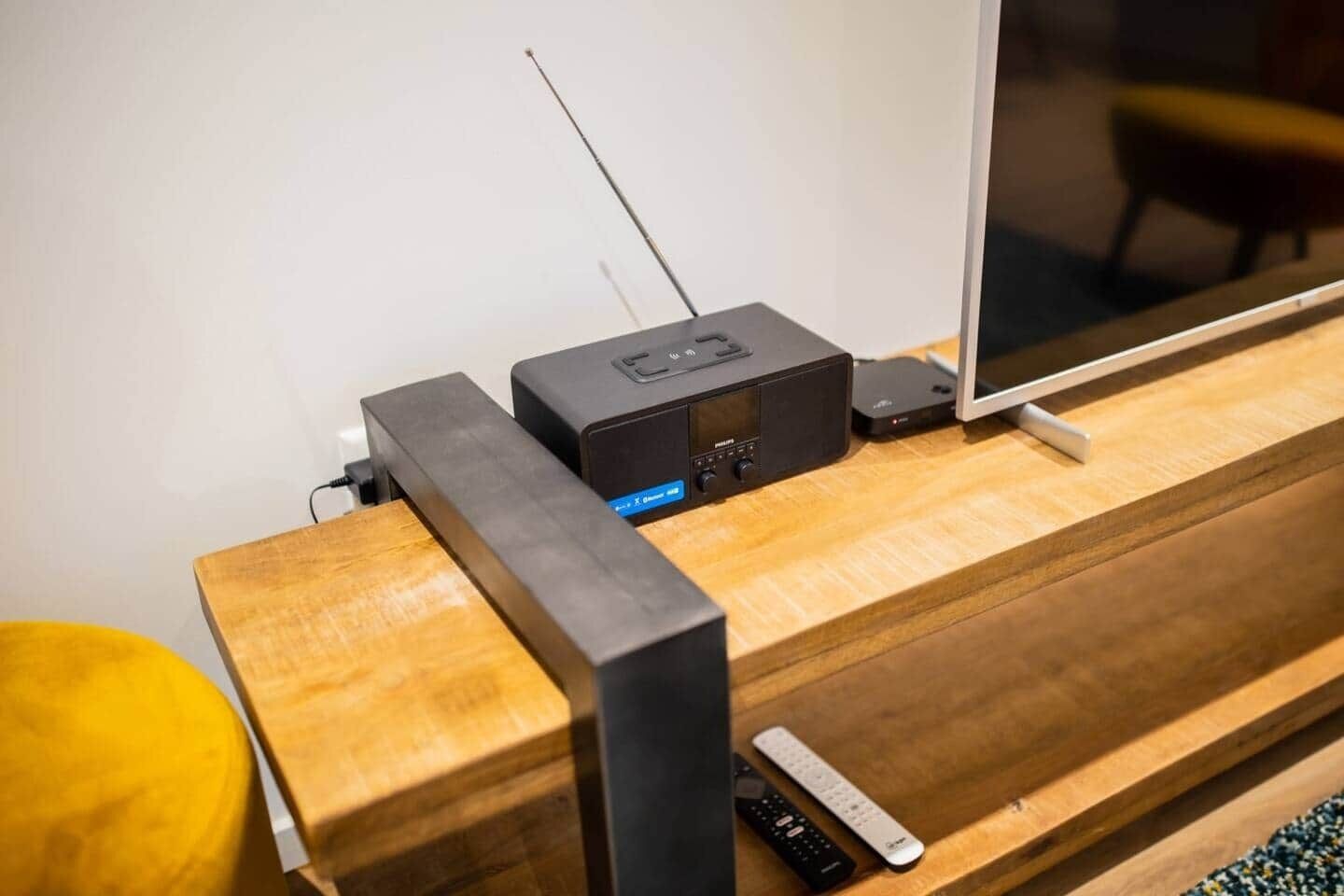 Et trætvbord med en sort elektronisk enhed, en fjernbetjening og et kabel.