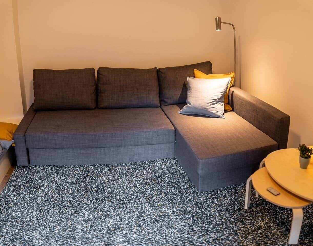 Uma sala de estar moderna com um sofá seccional cinza, uma mesinha redonda e um abajur.