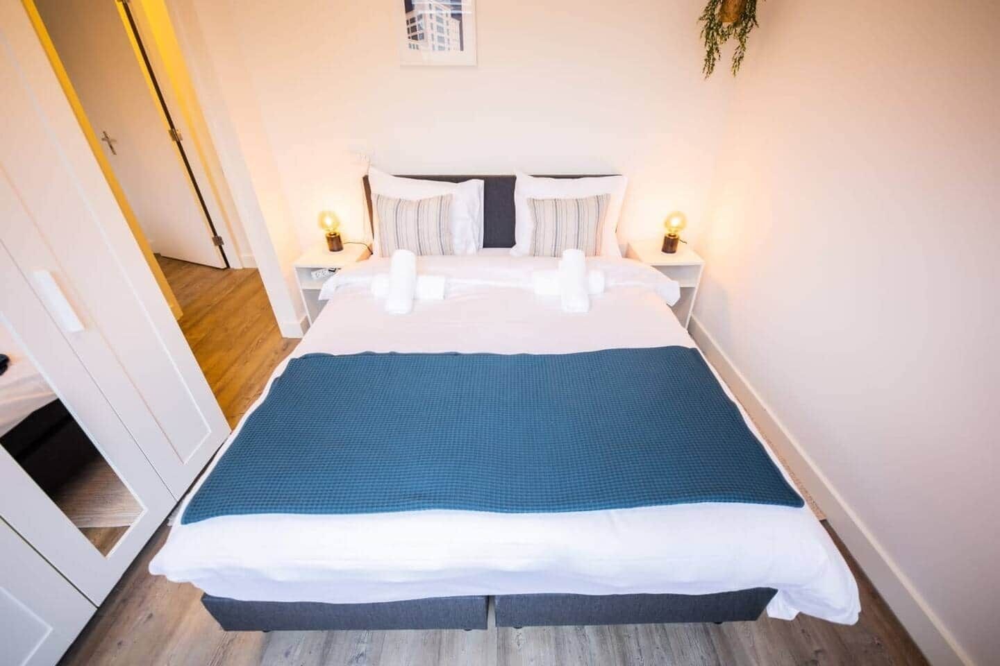 Een keurig opgemaakt bed met een blauw-witte dekbedovertrek, witte kussens en twee nachtlampjes.