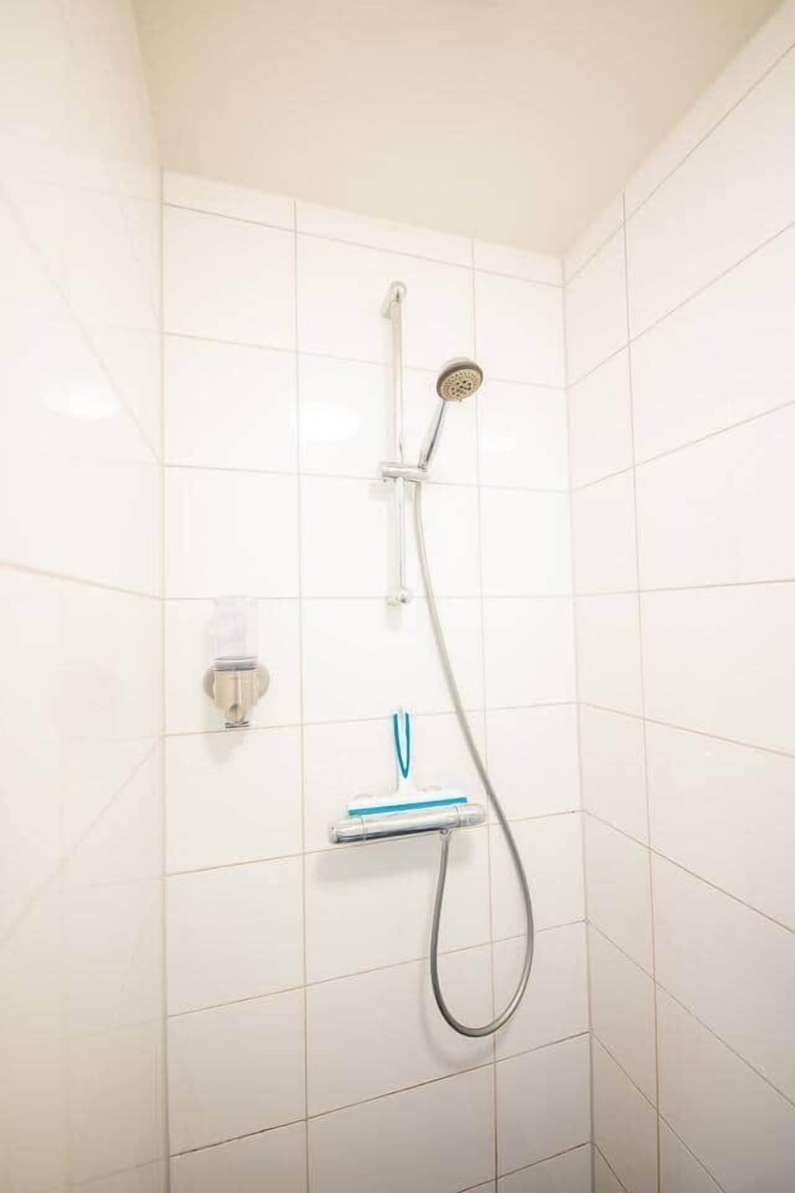 A shower with a handheld showerhead and a wall-mounted faucet.