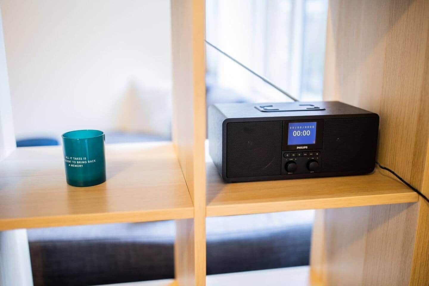 A Philips radio on a wooden shelf with a teal mug beside it.