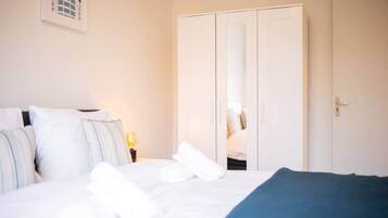 A hotel room with a bed, pillows, a bedside table with a lamp, and a wardrobe.