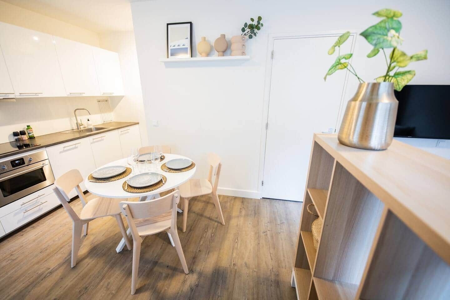 A modern kitchen with white cabinets, a built-in oven, and a dining area with a round table and chairs.