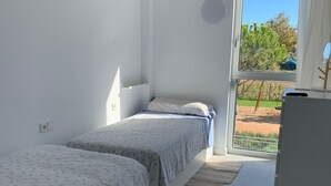 Ein Schlafzimmer mit zwei Betten, einer Schiebetür zu einem Außenbereich und einem kleinen Kühlschrank.