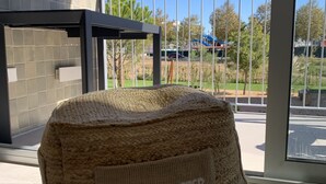 Ein gewebter Pouf mit dem Aufdruck "Life is better at the beach" auf einem Balkon mit Blick auf einen Parkplatz und Bäume.